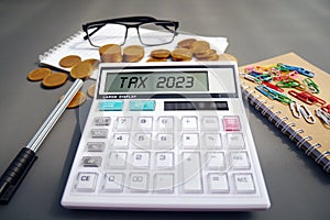 Word Tax 2023 on the calculator. Business and tax concept .Calculator, currency, book, tax form, and pen on gray desk table.