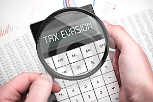 The word tax evasion is written on the calculator. Business man holding a calculator in his hand