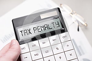 The word TAX PENALITY is written on the calculator. Business man holding a calculator in his hand