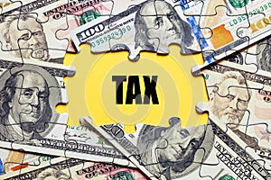 The word tax surrounded by puzzle pieces with dollar bill money. Tax payment or taxation