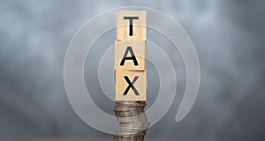 Word TAX written on wooden cubes on stacked coins on dark background. pay taxes concept - wooden blocks on coin stacks