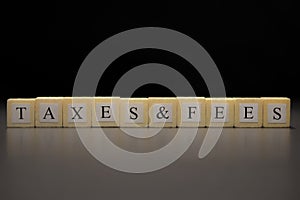 The word TAXES & FEES written on wooden cubes isolated on a black background