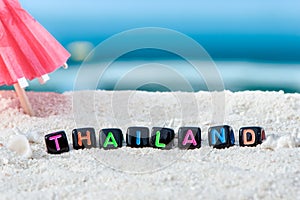 Word Thailand is made of multicolored letters on snow-white sand against the blue sea.