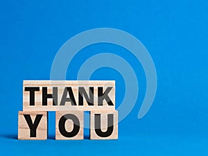 Word thank you written on wooden blocks isolated on blue background.