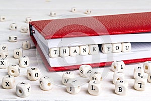 Word Thank you written in wooden blocks in red notebook on white