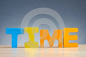 Word TIME spelled using wooden alphabet on desk over gently lit dark background