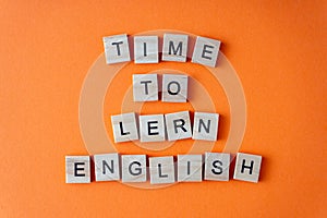 Word time to learn English. Motivation. The phrase is laid out in wooden letters top view. Motivation. Orange flat lay