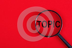 The word TOPIC is written on a magnifying glass on a red background