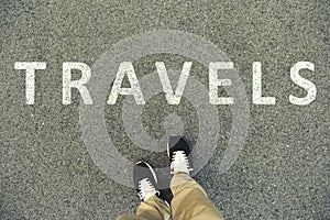 Word travels written on an asphalt road. Top view of the legs an