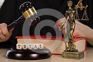 Word TRIAL composed of wooden dices. Wooden gavel and statue of Themis in the background