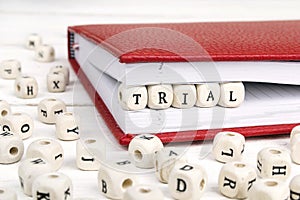 Word Trial written in wooden blocks in notebook on white wooden photo