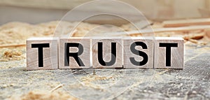 The word TRUST is written on wooden cubes. Wooden cubes lie on the table with sawdust and wooden blocks. Designed to promote your