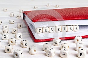 Word Trustee written in wooden blocks in red notebook on white w