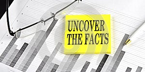 Word UNCOVER THE FACTS on a yellow sticky on the chart background