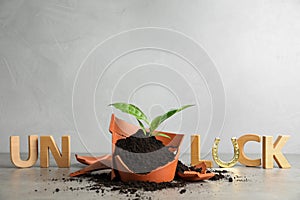 Word UNLUCK made of wooden letters and plant in broken pot on stone table