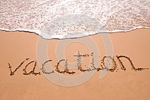 Word Vacation hand written in the sand with a sea wave. Close up sand texture on beach in summer