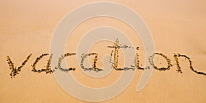 Word Vacation hand written in the sand with a sea wave. Close up sand texture on beach in summer