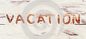 Word `vacation` written by sand on the wooden planks