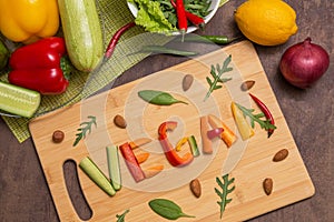 Word Vegan written with different raw vegetables, fruits, nuts and greens on wooden cutting board