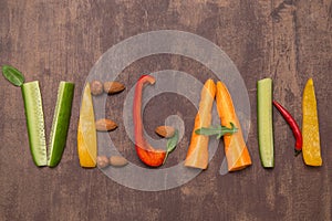 Word Vegan written with letters from different vegetables, fruits, nuts on rustic wooden background. Organic vegan food