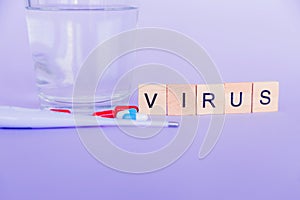 The word virus composed of wooden blocks, pills, a thermometer and a glass of water on a purple background