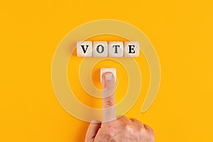 The word vote written on wooden cubes with a male hand pushing the voting button. Online voting concept in politics or business