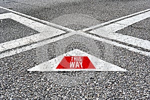 The word this way written on asphalt road with direction arrows