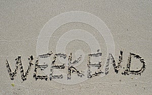 The word weekend written on sand.