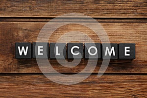 Word Welcome made of black cubes on wooden background, top view