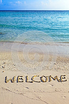 Word welcome is written on sand on oceanside