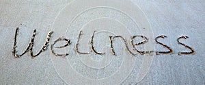 Word Wellness written on the sand near the sea.