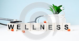 The word wellness is written on wooden cubes near a stethoscope on a wooden background. Medical concept