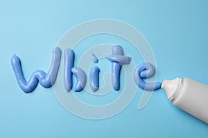 Word White written with toothpaste and tube on light blue background, flat lay