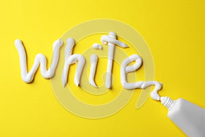 Word White written with toothpaste and tube on yellow background, top view