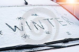 Word Winter written with finger on a snowy windshield of a car
