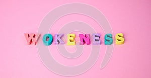 the word wokeness laid with colorful wooden letters against pink background