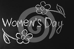 Word Women`s Day written in white chalk on a black chalkboard