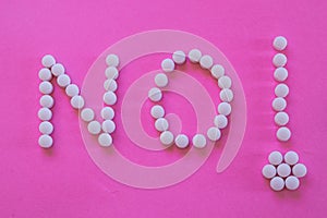 Word Word `NO` and an exclamation made with white pills  on pink background.