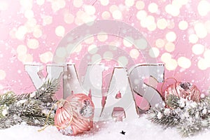 Word Xmas made from wooden letters, branches fur trees, decorations against pink textured wall.