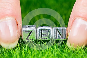 Word ZEN written in metal letters laid on grass and held between the fingers of a woman. Concept of wellness background