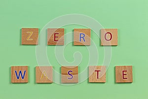 The word ZERO WASTE, spelt with wooden letter tiles over light green background. Top view