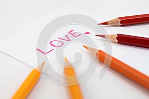 Wording Love in pink color with little heart on the small paper , encircle with color pencils in warm tone