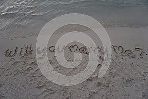 Wording `Will you marry me?` which hand writing on sand with sea background