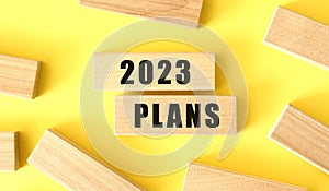 The words 2023 PLANS is written on a wooden blocks on a yellow background.