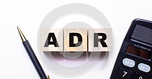 The words ADR Alternative Dispute Resolution is written on wooden cubes between a pen and a calculator on a light background