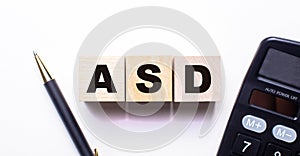 The words ASD Autism Spectrum Disorder is written on wooden cubes between a pen and a calculator on a light background