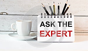 The words ASK THE EXPERT is written in a white notepad near a white cup of coffee on a light background