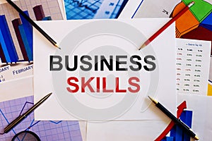 The words BUSINESS SKILLS is written on a white background near colored graphs, pens and pencils. Business concept