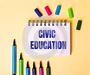 The words CIVIC EDUCATION written in a white notebook on a beige background near multi-colored markers