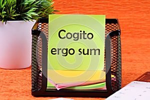 The words Cogito Ergo Sum or I think Therefore I Am on a sticker in a stand on an orange background
